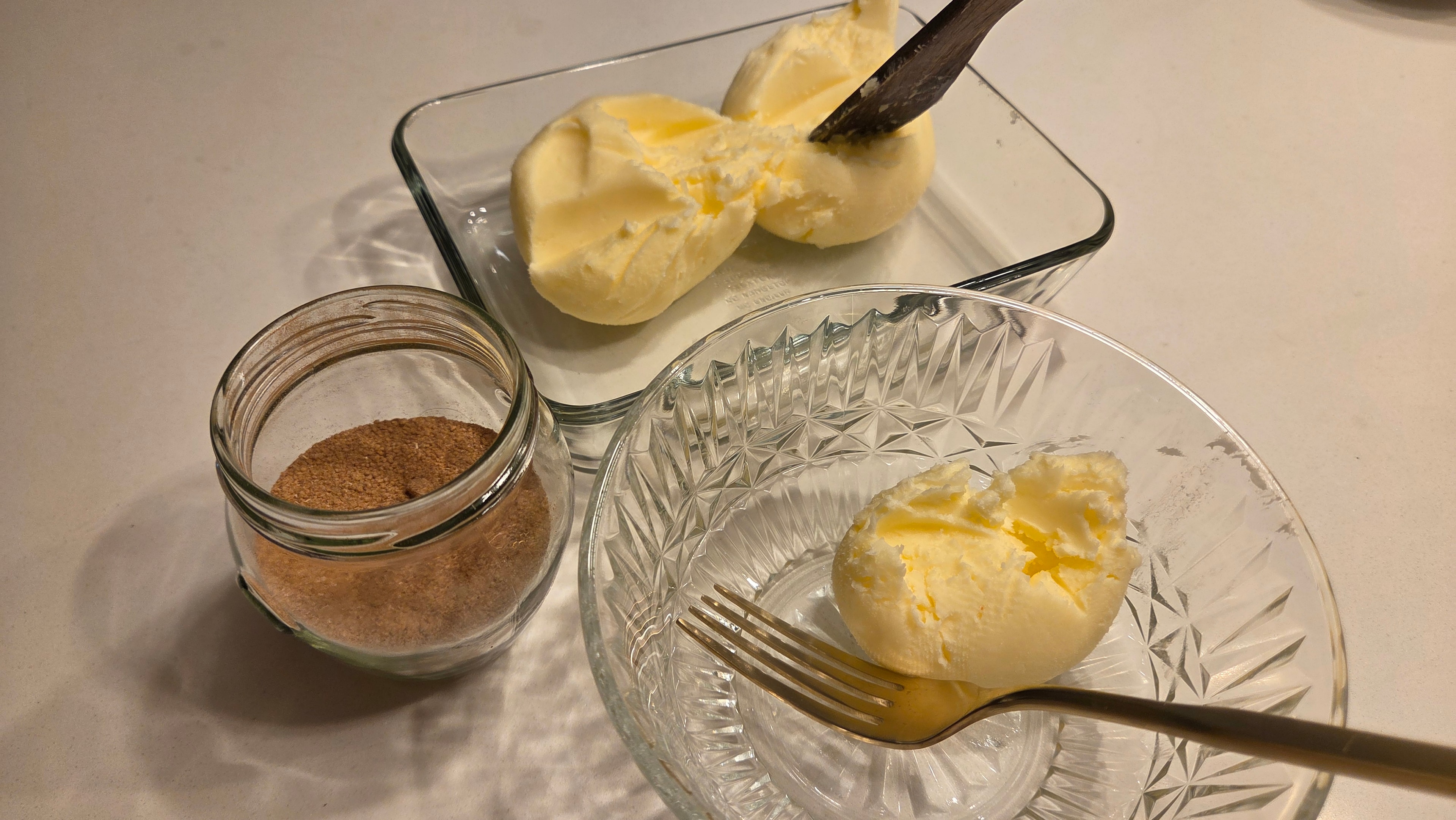 Homemade butter portions in glass dishes alongside the cinnamon sugar jar and a fork, ready to combine