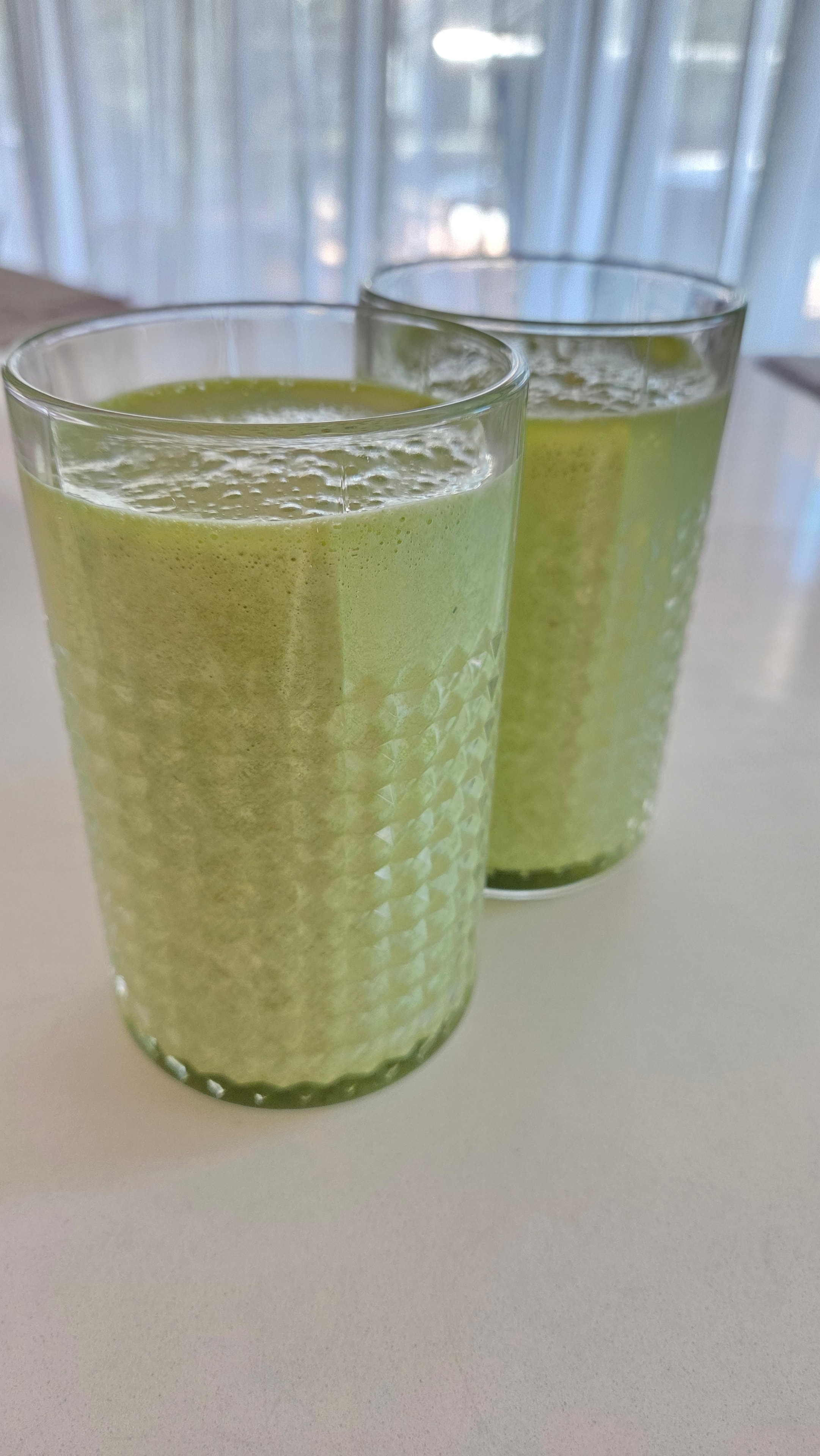 Two textured glasses filled with vivid green cucumber matcha smoothie, side view