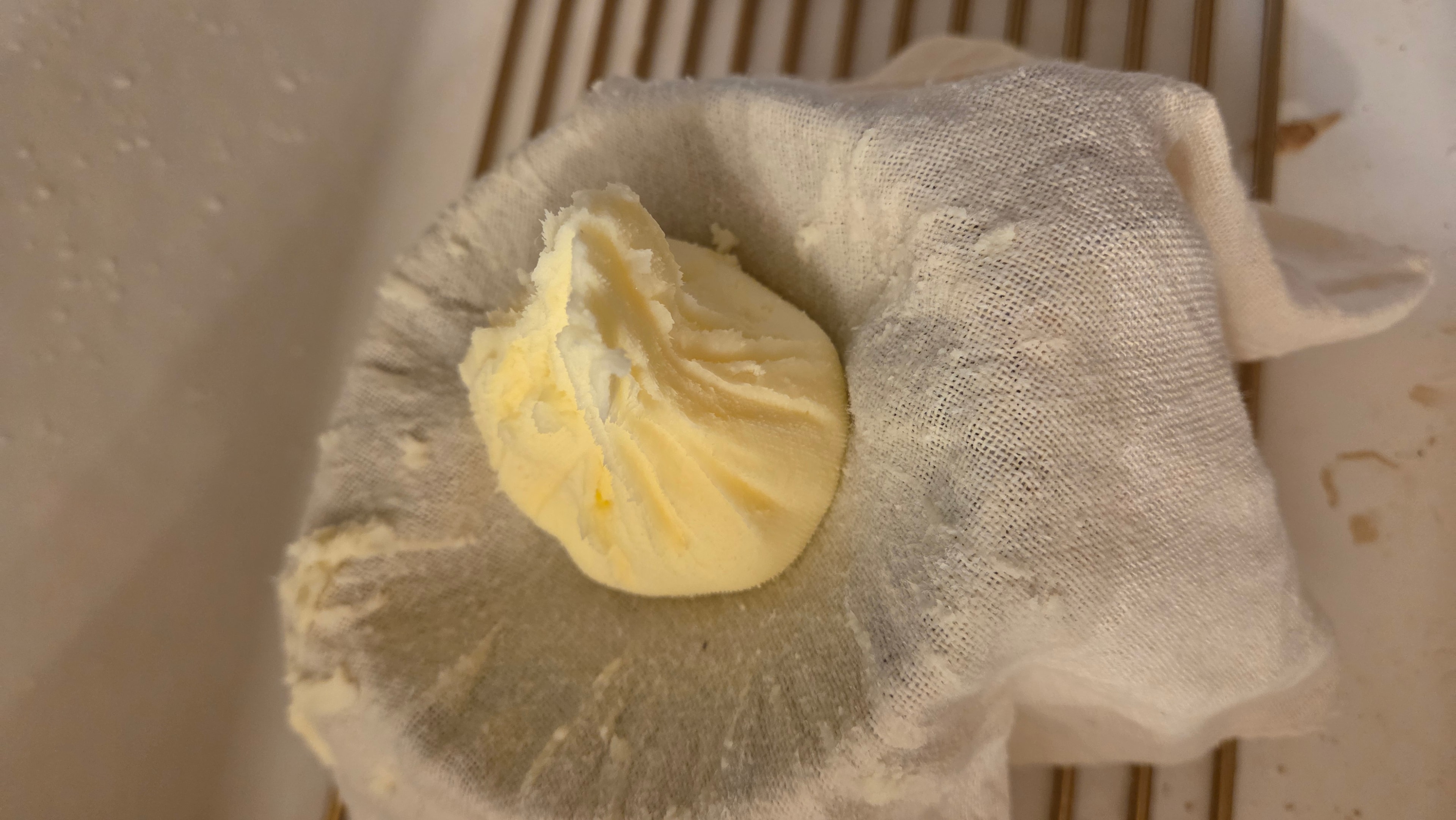 Butter wrapped in cheesecloth being pressed to remove the last of the water