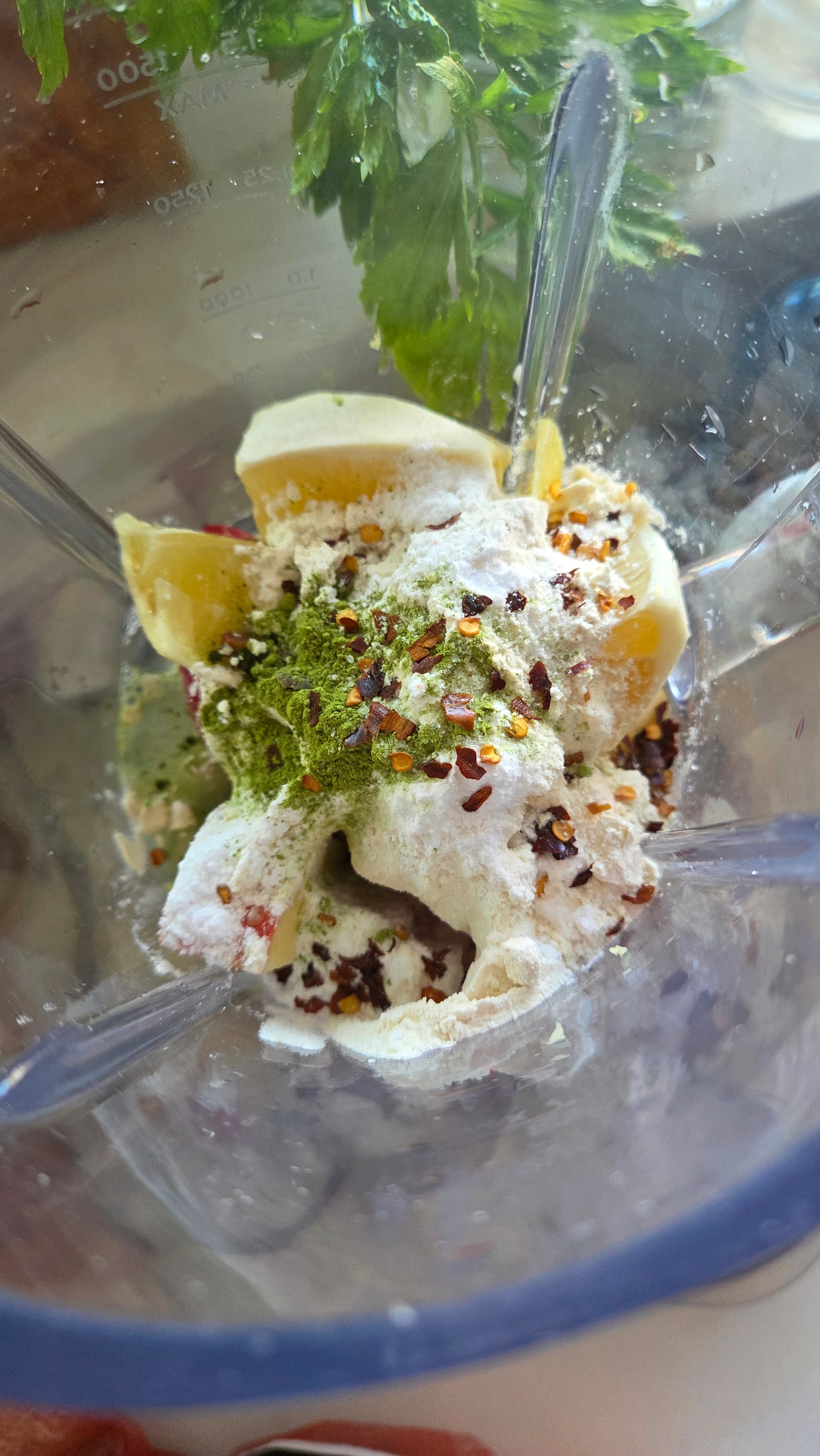 Blender bowl loaded with lemon, ginger, whey protein, matcha, crushed chilli and spinach ready to blend