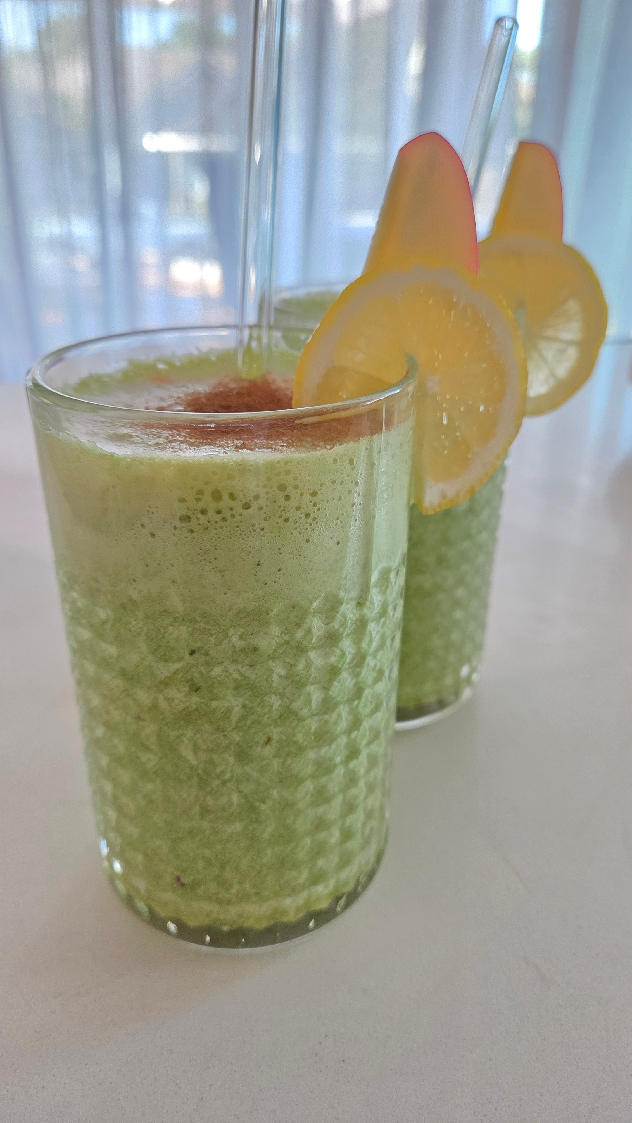Two tall glasses of lemon apple spinach matcha smoothie with lemon and apple slice garnish