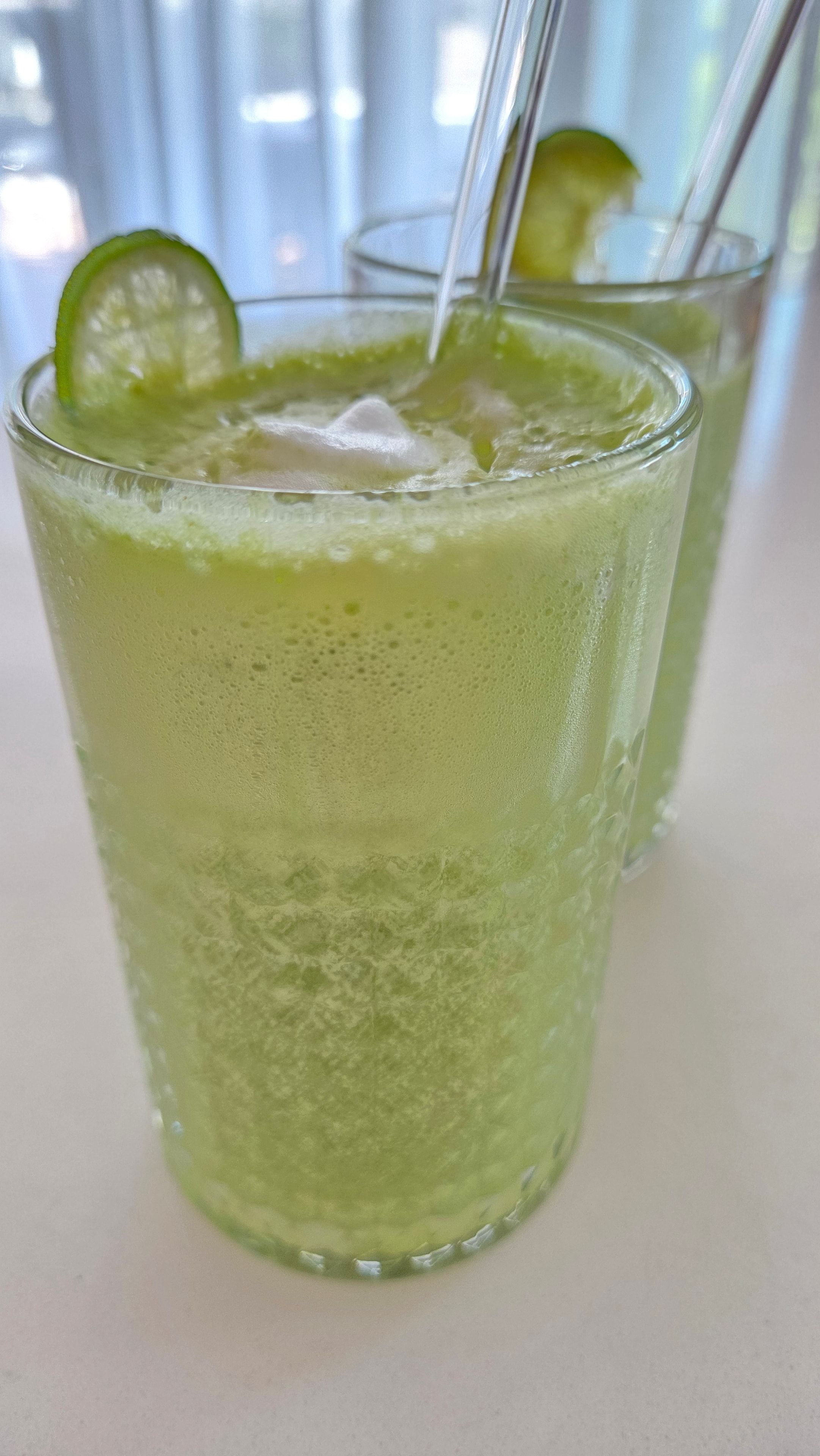 Two tall glasses of lime lemon spinach matcha smoothie with cold vanilla foam and lime slice garnish, side view