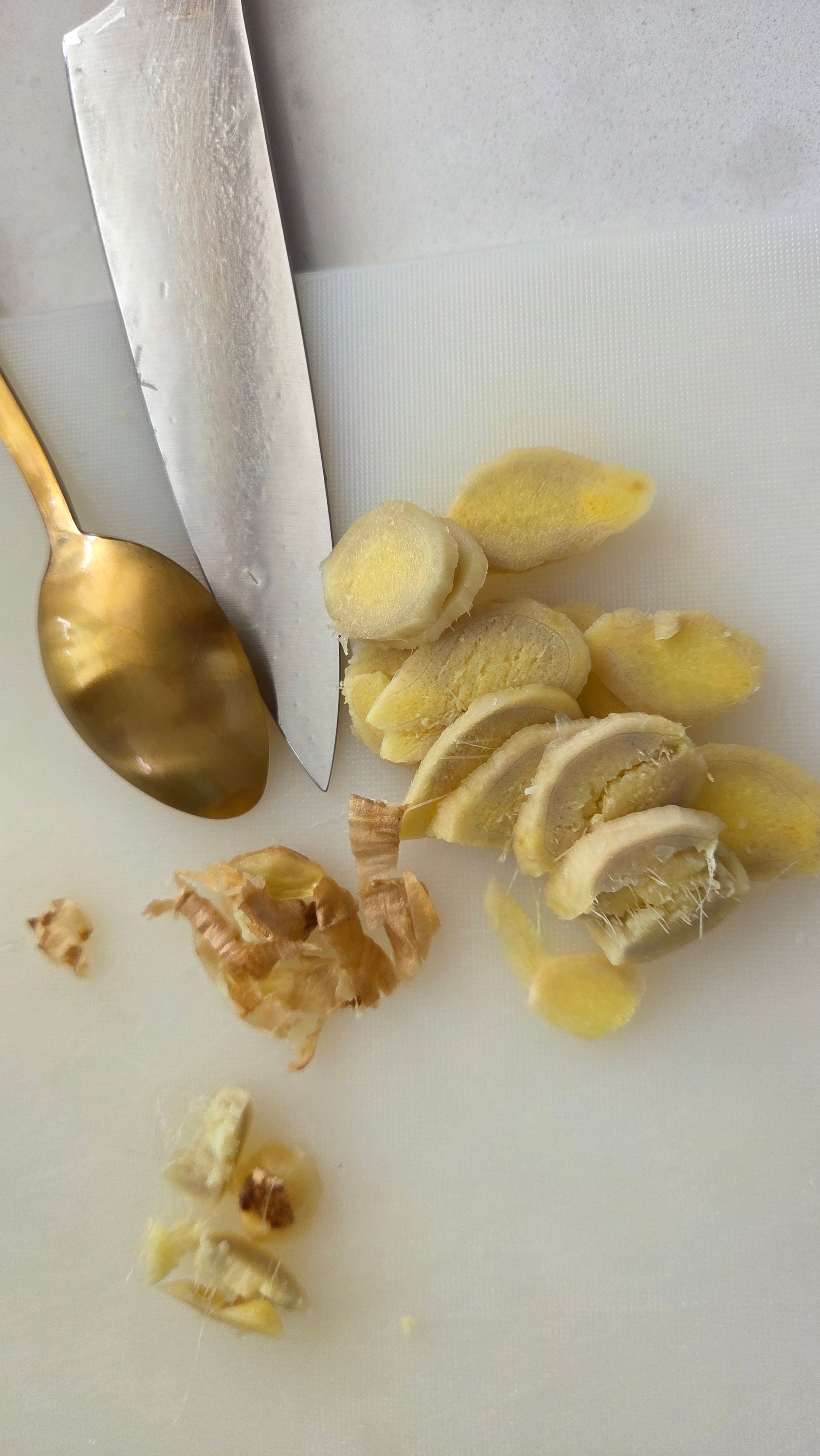 Fresh ginger scraped with a spoon and sliced thinly across the grain on a white board