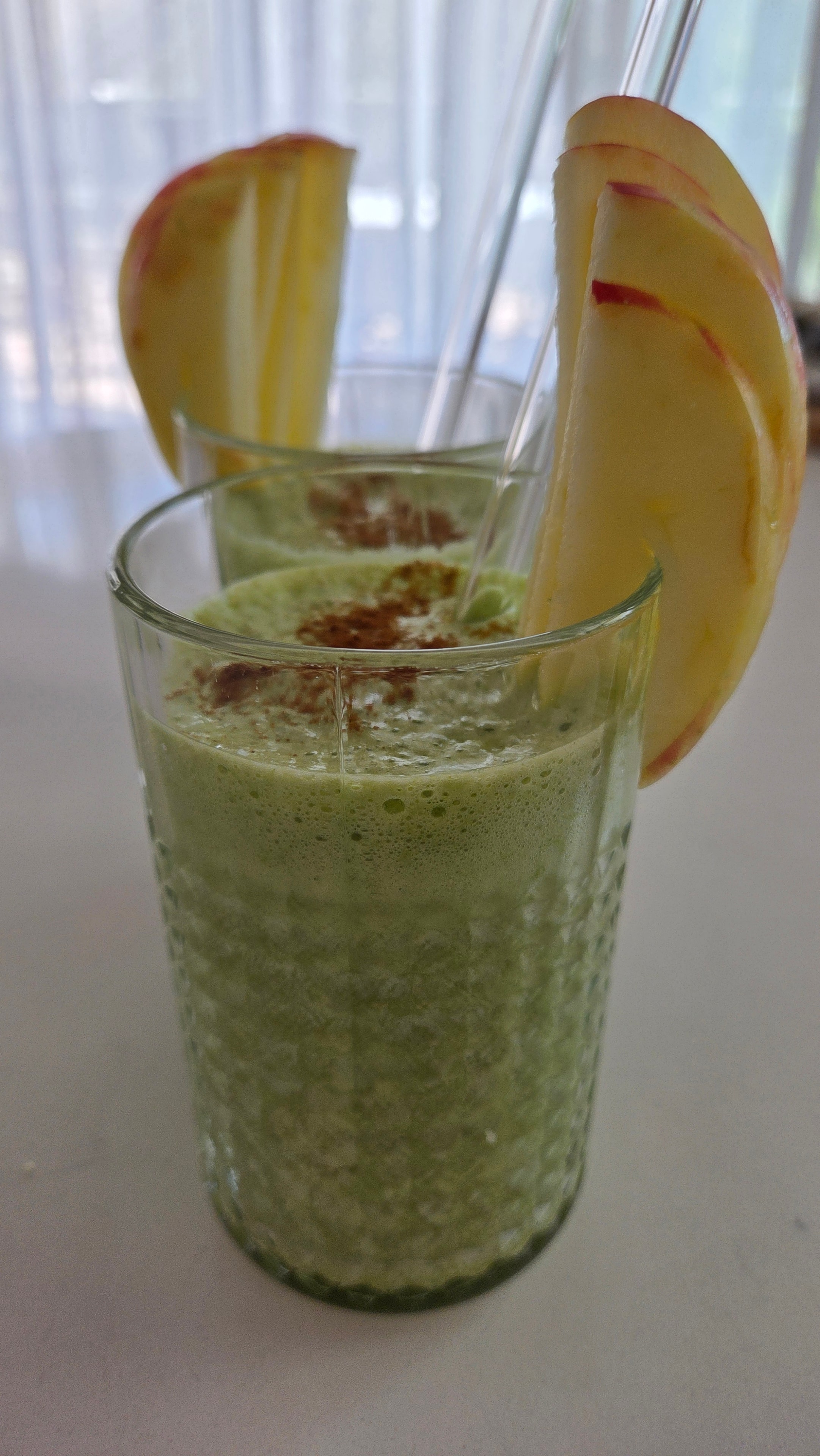 Two tall glasses of matcha apple ginger smoothie with cinnamon dusting and apple slice garnish