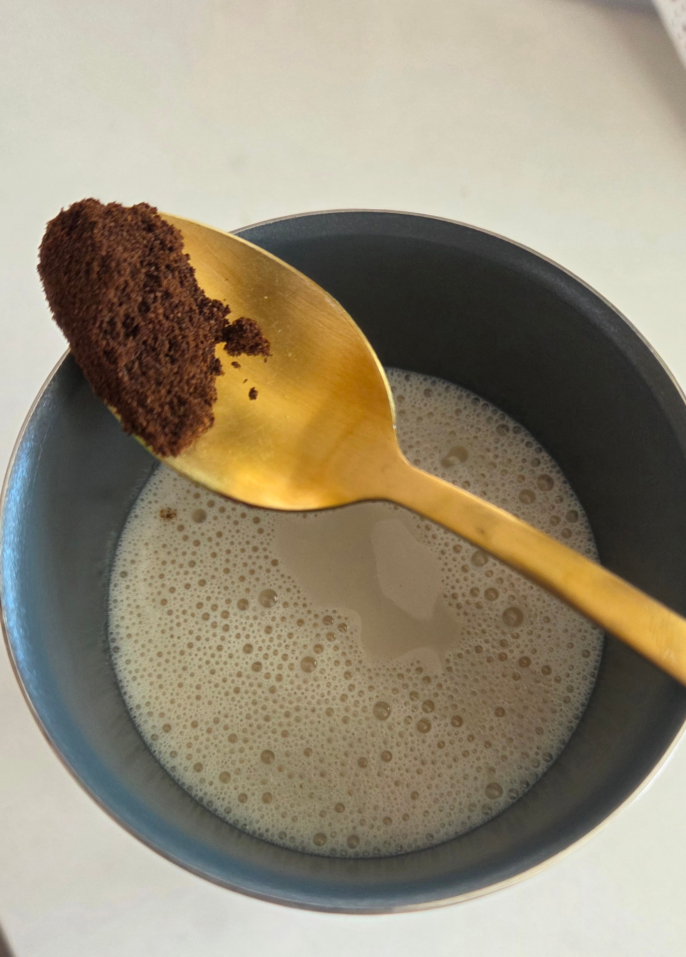 Cold vanilla oat milk foam being prepared in a dark bowl with a gold spoon
