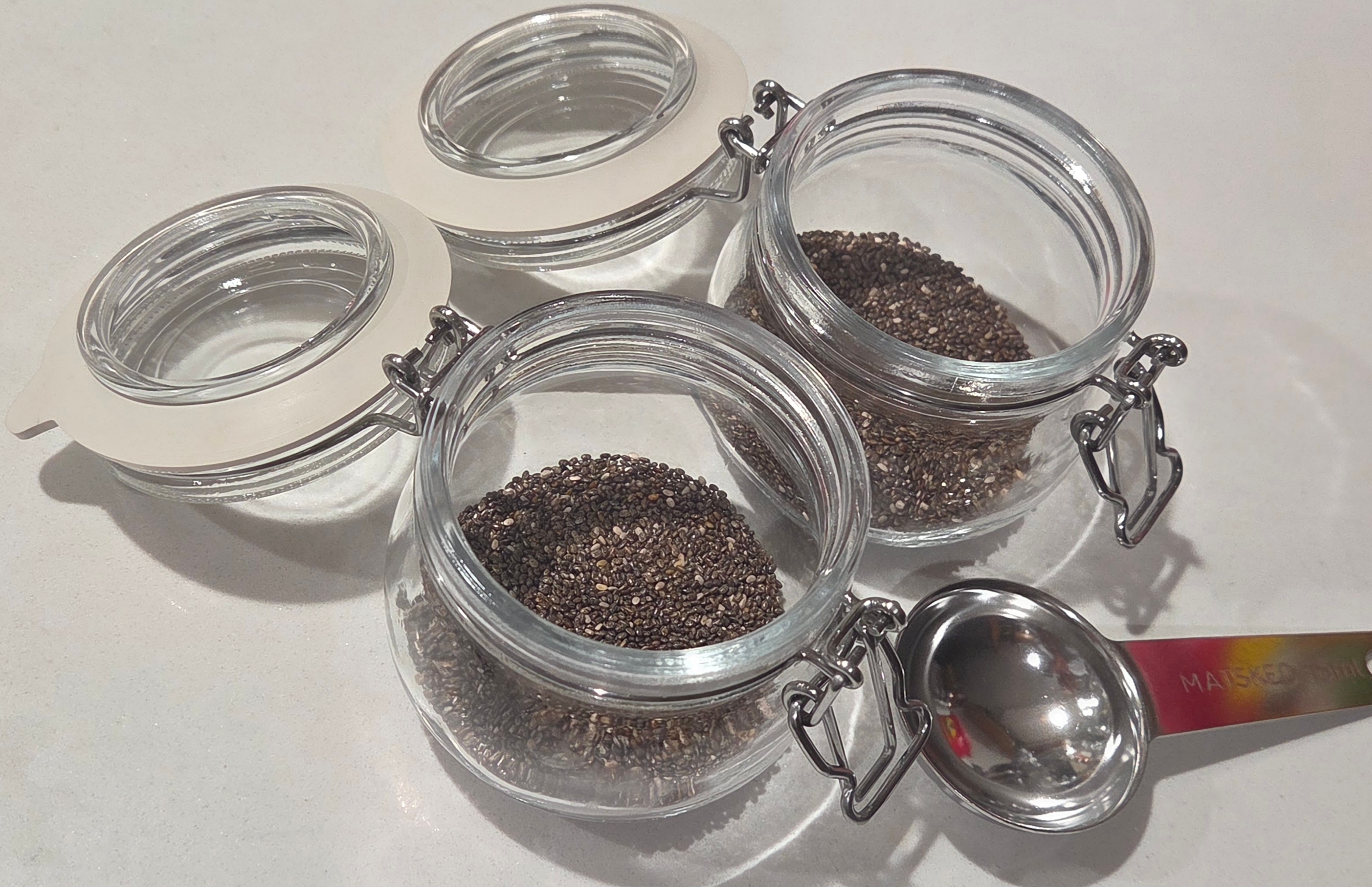 Two empty glass clip-top jars with chia seeds measured out, and a measuring spoon alongside