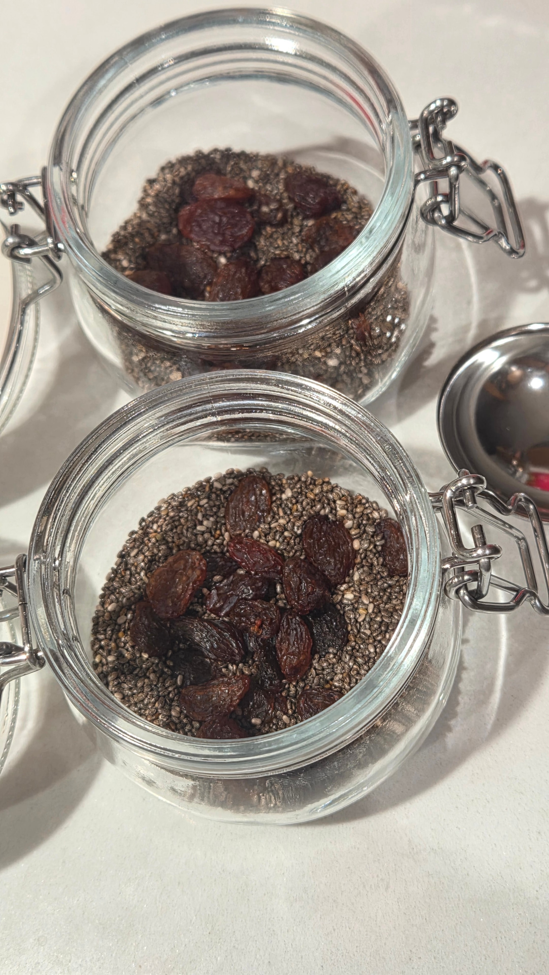 Glass jars with chia seeds and raisins layered inside, measuring spoon resting beside them