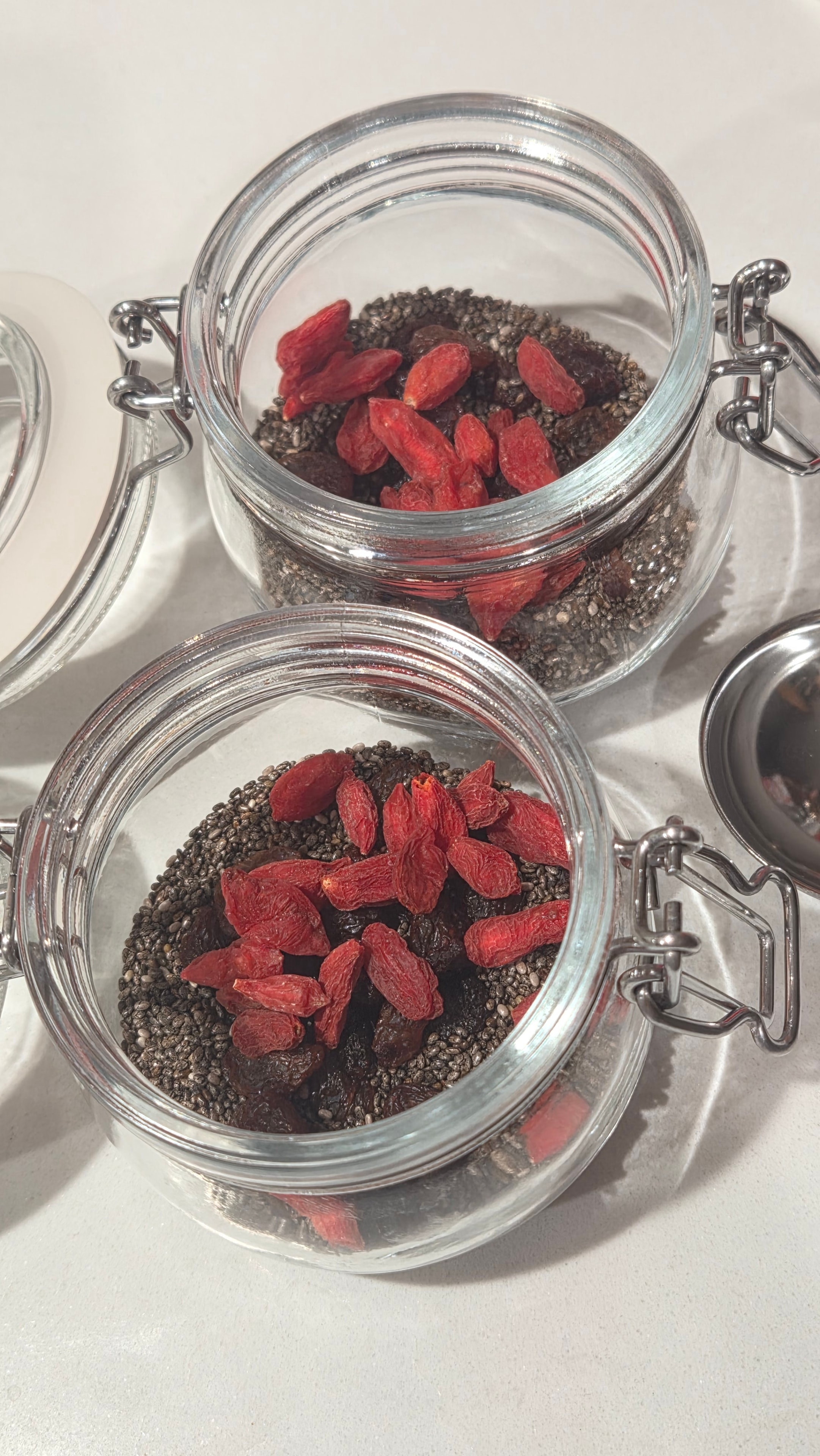 Jars with chia seeds, raisins, and bright red goji berries layered on top