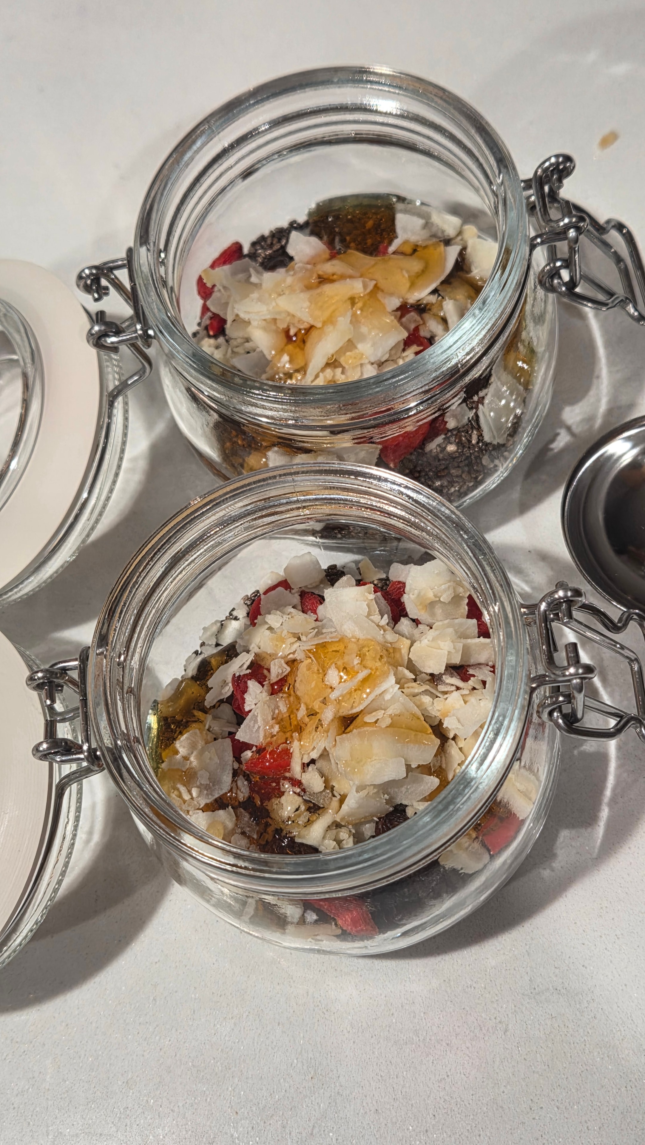 Jars with all dry ingredients including coconut flakes and honey drizzled on top, viewed from above