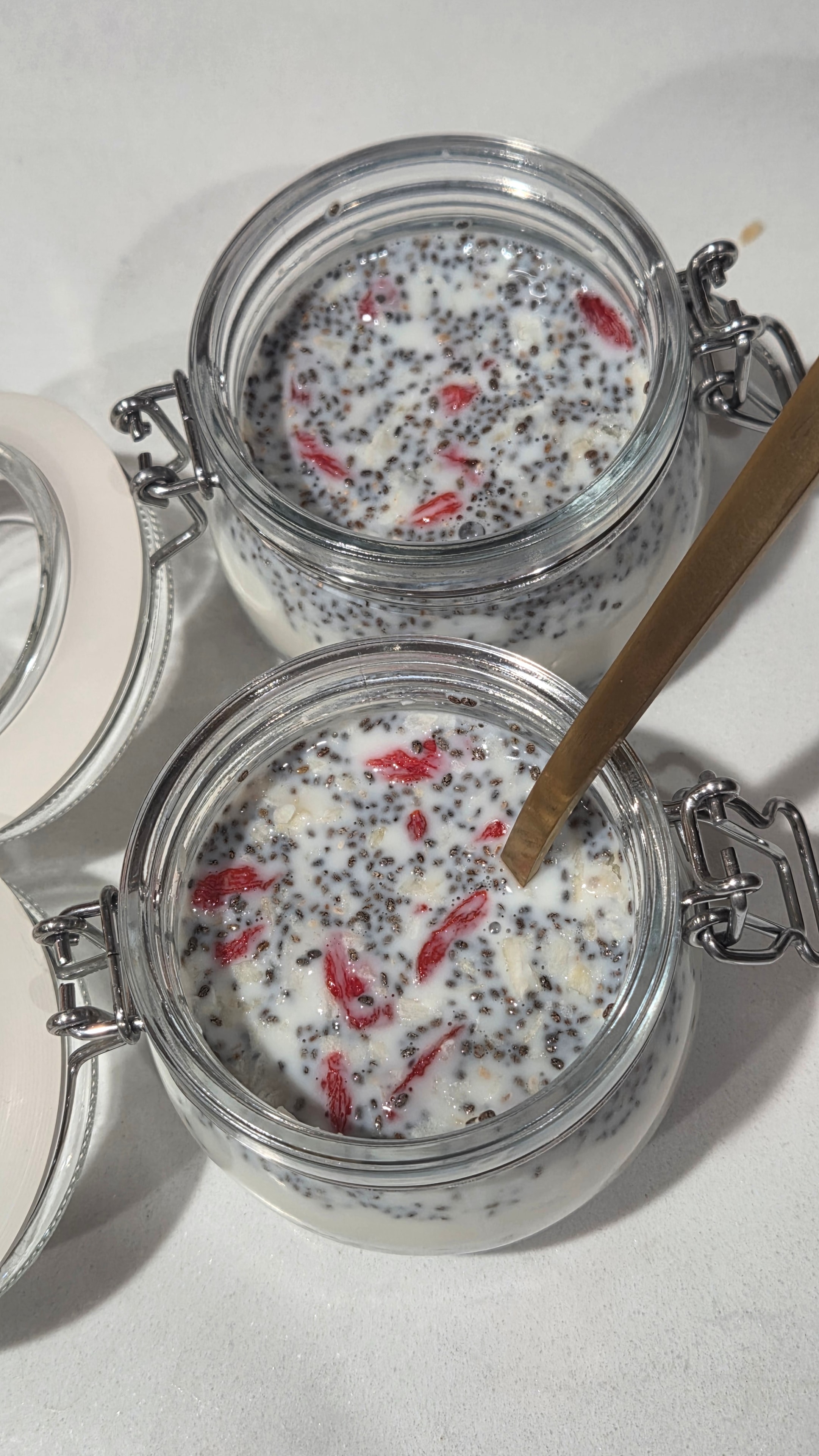 Jars after stirring with a gold spoon — milk and chia seeds and goji berries fully combined