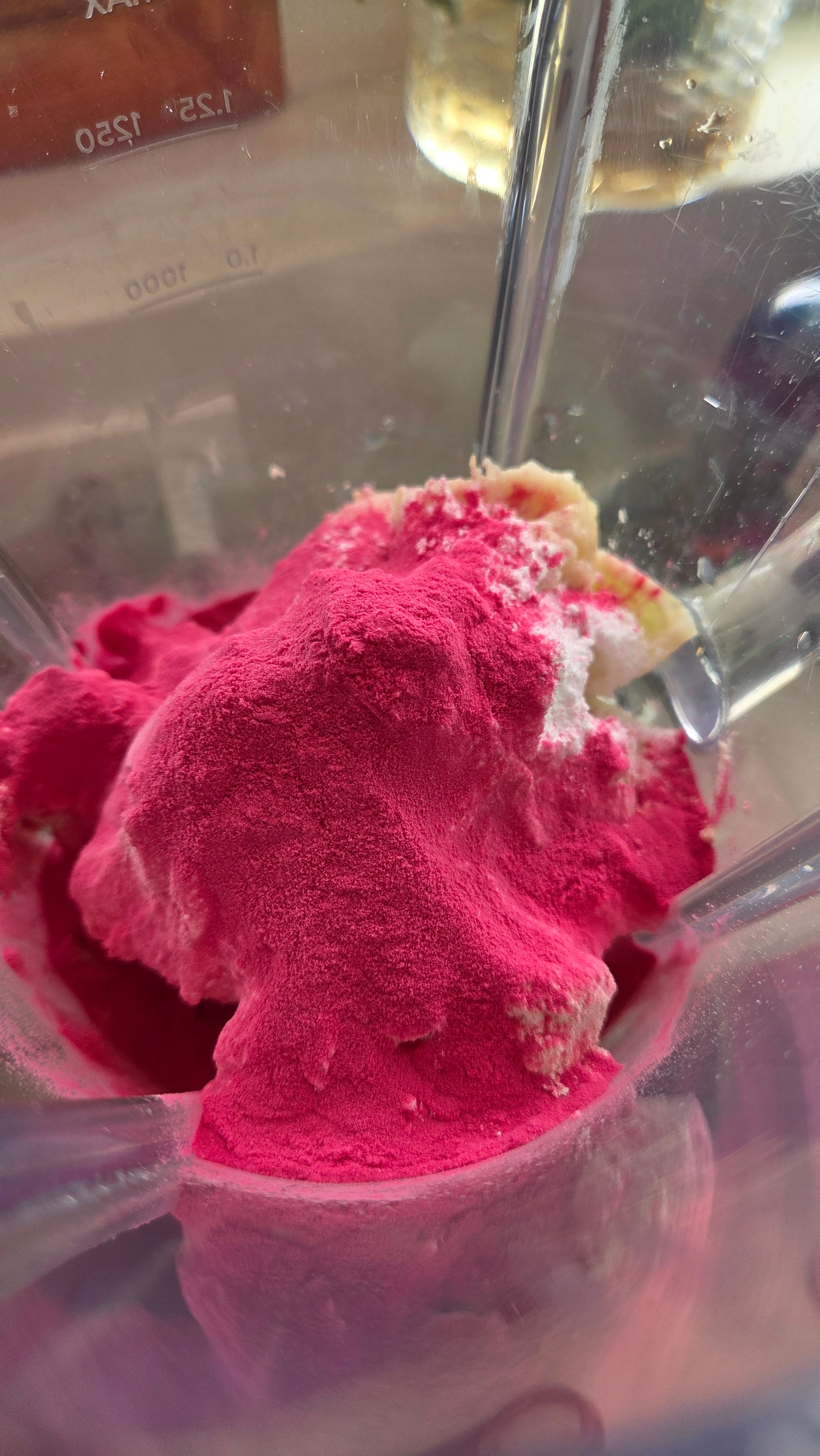 Pink pitaya powder added to the blender — vivid magenta against the pale fruit base