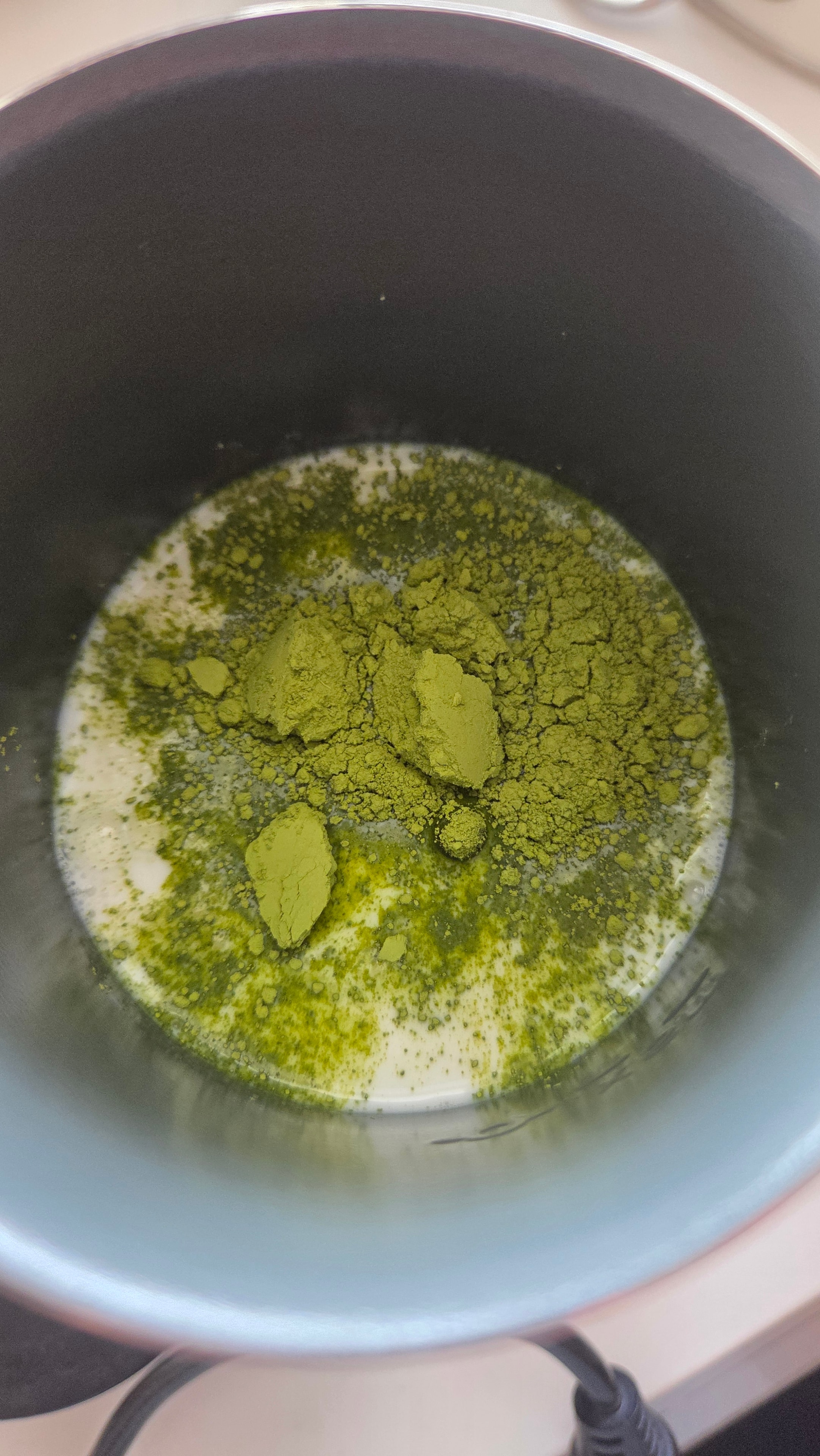 Matcha powder added to the milk in the frother — green powder on white milk