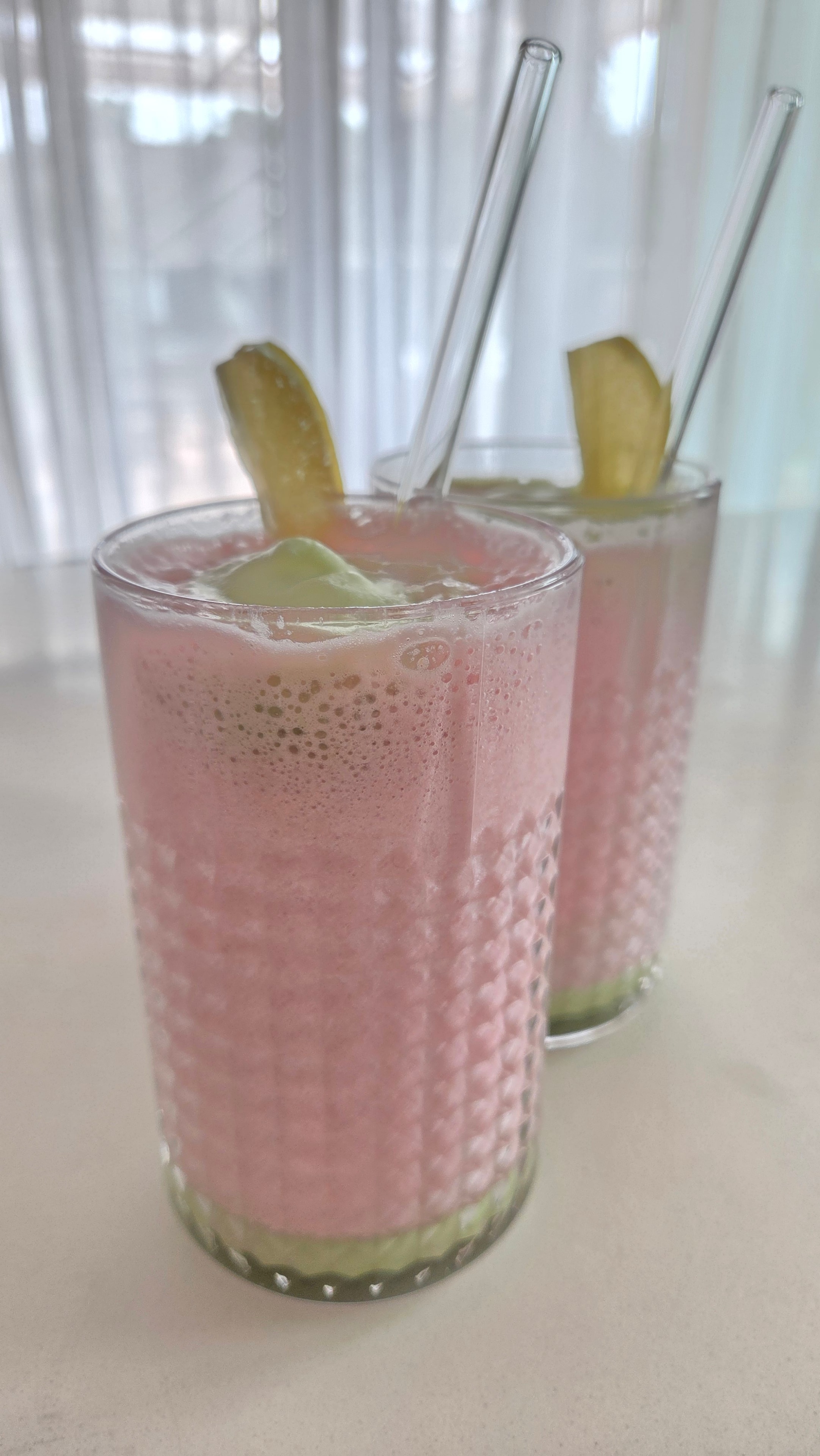 Two glasses of pink pitaya smoothie with lemon garnish before the foam is added