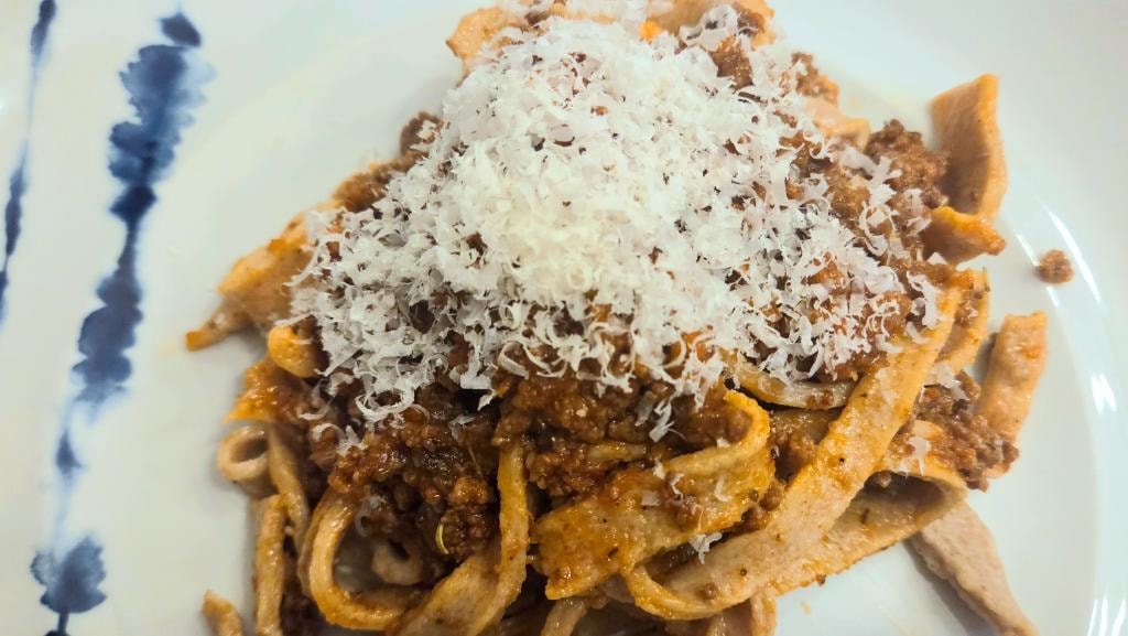 Handmade whole wheat pasta served with meat sauce and grated cheese
