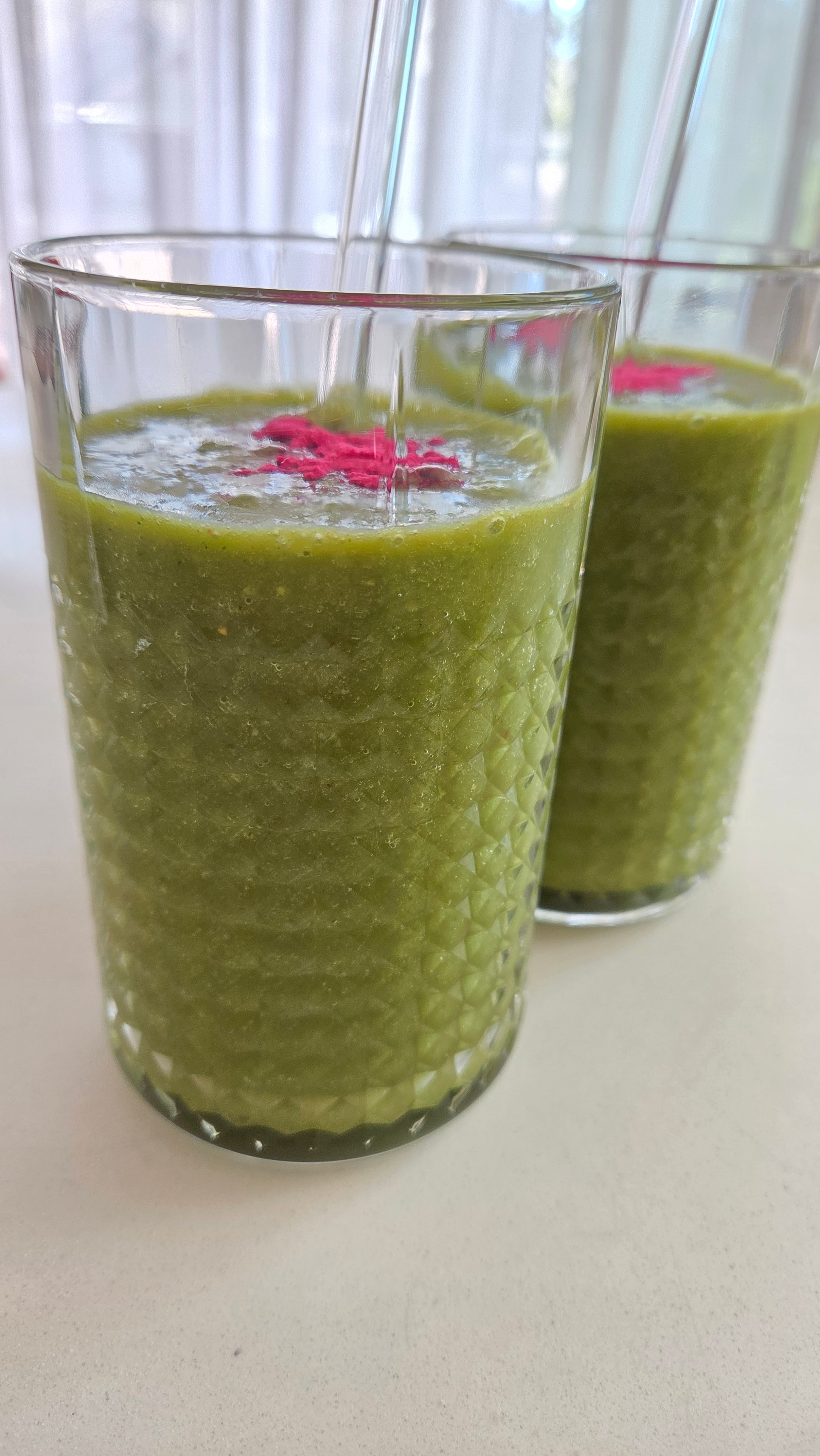 Two tall glasses filled with vivid green smoothie — the pitaya powder just dusted on top, ready to serve